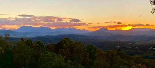 a sunset over a mountain range with trees in the foreground at KooralBnB in Kooralbyn
