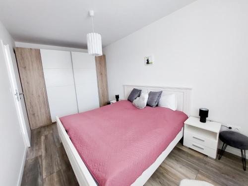 Biała sypialnia z różowym łóżkiem i biurkiem w obiekcie Juhar Apartman w mieście Kőszeg