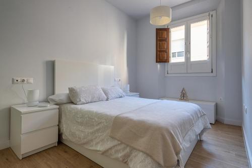 een witte slaapkamer met een bed en een raam bij Puerta Real Centro Apartment in Granada