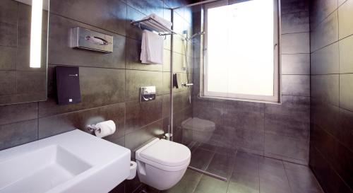 a bathroom with a toilet and a sink and a window at Home Hotel Folketeateret in Oslo