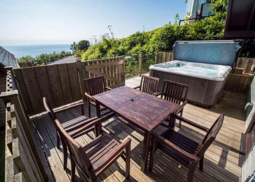a wooden table and chairs on a deck with a hot tub at Leonards Cove in Stoke Fleming