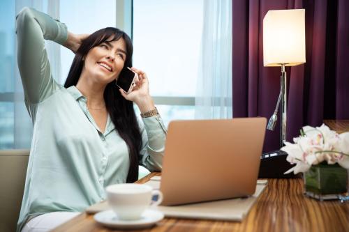 a woman sitting at a desk talking on a cell phone at Pullman Dubai Jumeirah Lakes Towers in Dubai