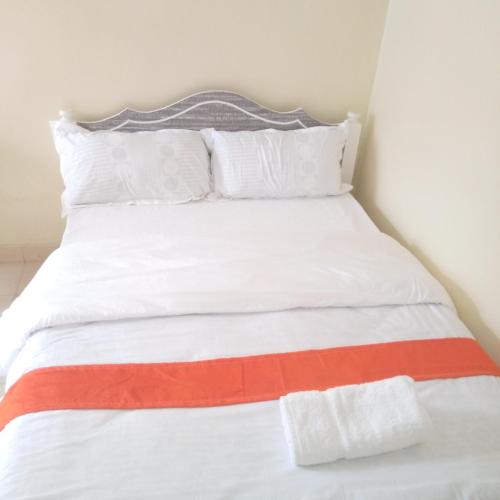 ein weißes Bett mit orangefarbenen und weißen Kissen in der Unterkunft Luna Light Guest House in Naivasha