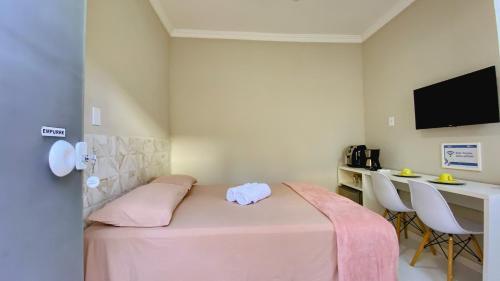 um quarto com uma cama rosa, uma secretária e uma televisão em Kalug - Suíte CASAL independente em Guest house em Ilhéus