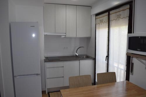 cocina con armarios blancos, mesa y sillas en Apartamento Arturo Soria, en Madrid