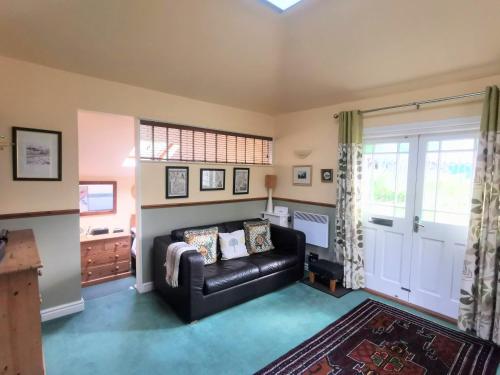 a living room with a black leather couch and a window at Rose Cottage, Meathop Grange in Grange Over Sands