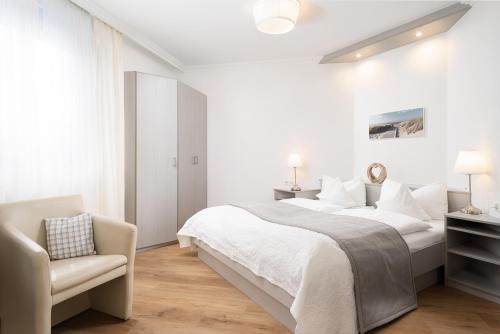 a white bedroom with a bed and a chair at Hotel Haus am Park in Borkum