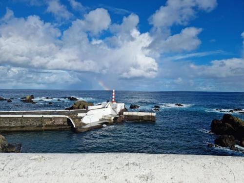 Ein Leuchtturm im Ozean mit einem Regenbogen am Himmel in der Unterkunft "Apartamentos do Farol" com vista para o mar in Santa Cruz das Flores