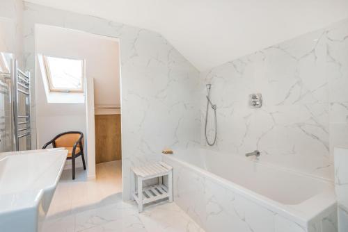 een witte badkamer met een bad en een stoel bij Red Kite Cottage in Petersfield