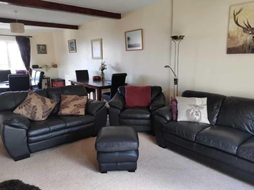 a living room with a black leather couch and a table at Spacious family & dog friendly home from home with sea views and private garden in Porlock