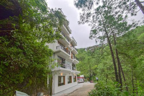 a white building in the middle of a forest at Hotel The Paal in Shimla