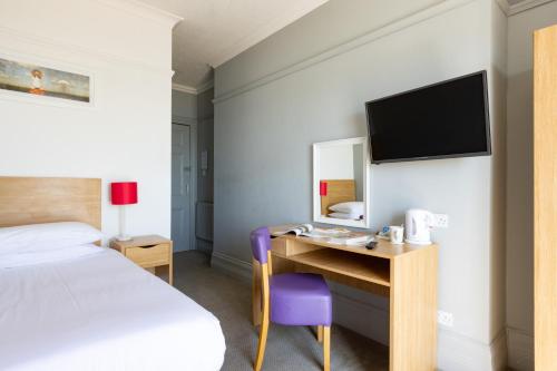 a bedroom with a bed and a desk with a tv at The Royal Hotel Weymouth in Weymouth