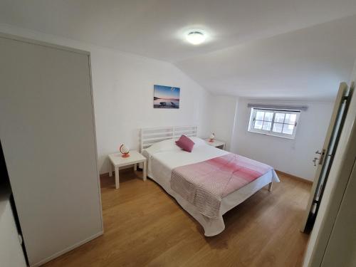 a white bedroom with a bed and a window at Alojamento Rosa in Nazaré