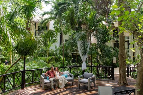 two people sitting in chairs on a deck with palm trees at The Reef Playacar Beach Resort & Spa-Optional All Inclusive in Playa del Carmen