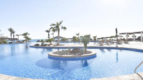 a swimming pool at a resort with palm trees and chairs at Luna Blanca Two Bedroom Unit by Kivoya in Puerto Peñasco