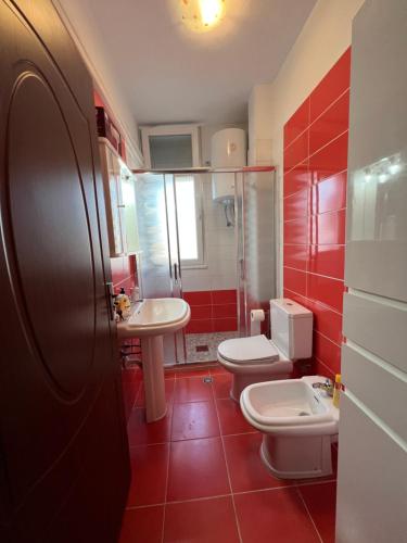 Baño rojo con 2 aseos y lavamanos en City Center Apartment in Shkoder, en Shkodër