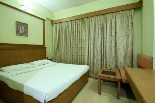 a bedroom with a bed and a table and a desk at Hotel Roopa in Mysore