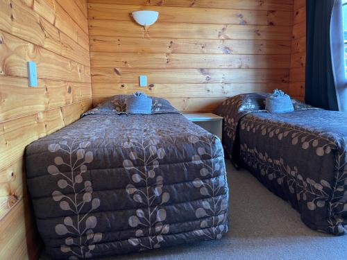 two beds in a room with wooden walls at Cedarwood Lakeside Motel & Conference Venue in Rotorua