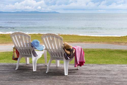 two chairs sitting on the beach with a hat on them at Golden Sand Beachfront Accommodation in Coopers Beach
