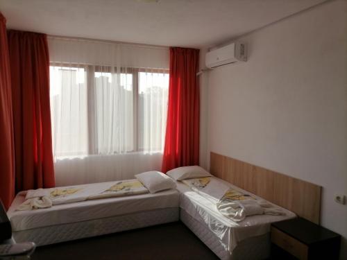 two beds in a room with a window with red curtains at Ivet Guest House in Obzor