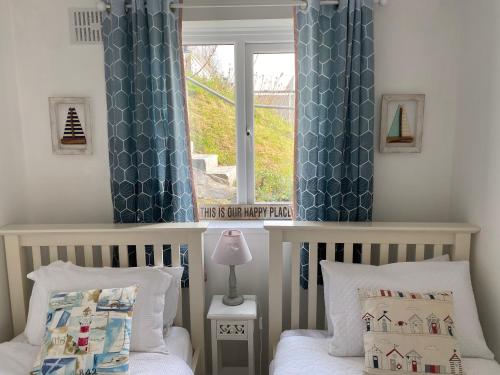 a bedroom with two beds and a window with blue curtains at Bay View, Millendreth Looe Cornwall in Looe