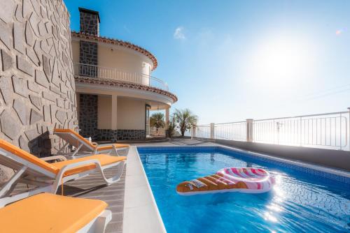 a swimming pool with chairs and a house at Sunnyside Villa in Arco da Calheta
