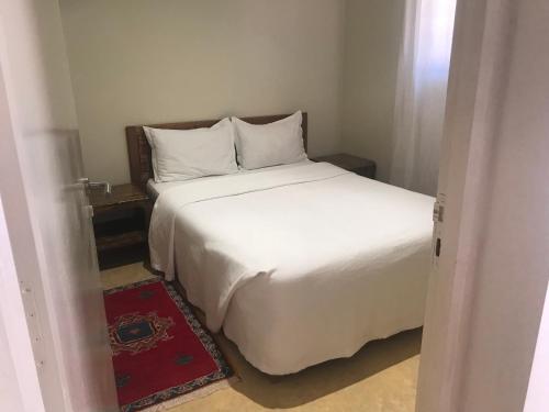 a bedroom with a white bed and a red rug at Côté Sud in Ouarzazate