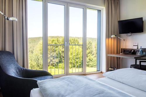 um quarto de hotel com uma cama e uma grande janela em BURGHOF - DAS HOTEL em Brombachtal