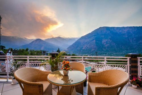 a table and chairs on a balcony with a view of mountains at Anand Vardhan Resorts in Manāli