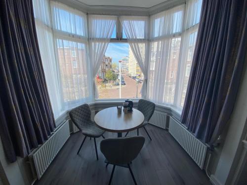 une table et des chaises dans une chambre avec une grande fenêtre dans l'établissement Hotel 't Sonnehuys, à Scheveningen