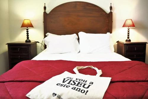 a bed with a red comforter with a sign if you wish to see at Casa Dos Gomes in Viseu