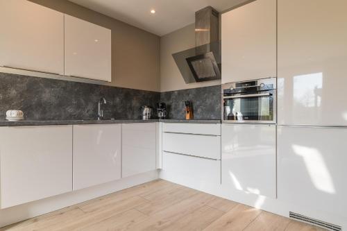 a kitchen with white cabinets and stainless steel appliances at Luxe appartement dichtbij strand en zee, in het hart van de bollenstreek in Noordwijkerhout