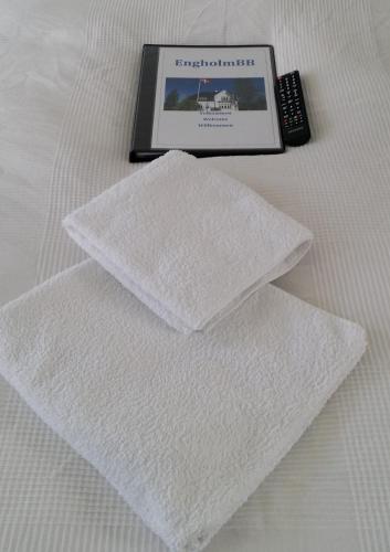 a pile of white towels on a bed with a remote control at EngholmBB in Odense