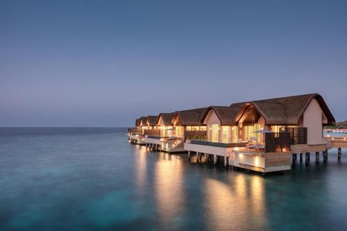 a row of houses on the water at night at JOALI BEING in Raa Atoll