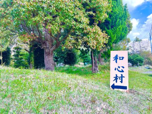 a sign in the grass next to a tree at 和心村ー古民家とグランピングと自然森山川海 in Minato