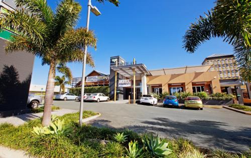 a street in front of a shopping center with palm trees at Nightcap at Hinterland Hotel Nerang in Gold Coast