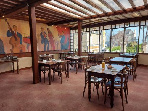 un restaurante con mesas y sillas de madera y ventanas en Hotel de Normandie, en Saint-Aubin-sur-Mer