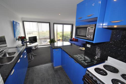 cocina con armarios azules, fregadero y microondas en Beachfront Apartments en Narooma