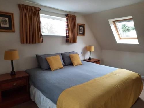 a bedroom with a large bed with two windows at Fir Tree Cottage in Blairgowrie