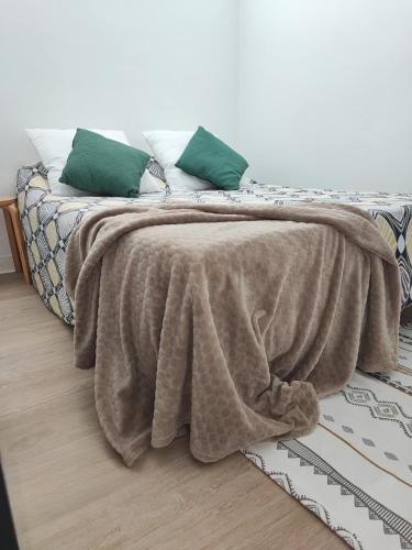 a bed with a brown blanket and green pillows on it at Joli T2 rénové et calme Quartier desrochers à Fort de France in Fort-de-France