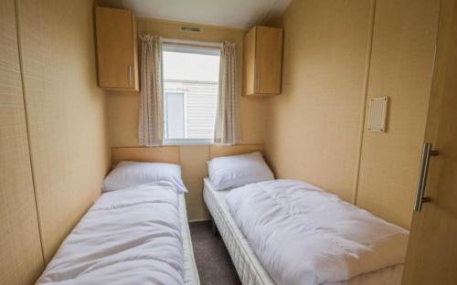 2 Betten in einem kleinen Zimmer mit Fenster in der Unterkunft Willerby Magnum in Clacton-on-Sea