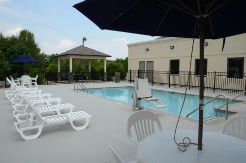 een zwembad met witte stoelen en tafels en een parasol bij Baymont by Wyndham Clarksville in Clarksville