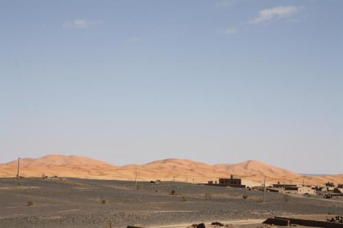 a desert scene with buildings and mountains in the distance at Sahara Desert Camp in Adrouine