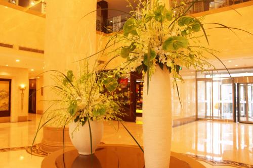 two white vases with flowers on a table in a lobby at Beijing Continental Grand Hotel in Beijing