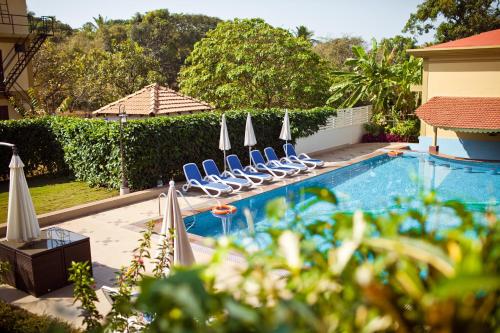 a swimming pool with lounge chairs and umbrellas at Cochichos Resort in Vagator