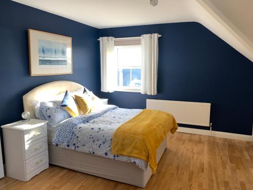 a blue bedroom with a bed and a window at Seascape on the edge of town: 4 beds all ensuite. in Belmullet
