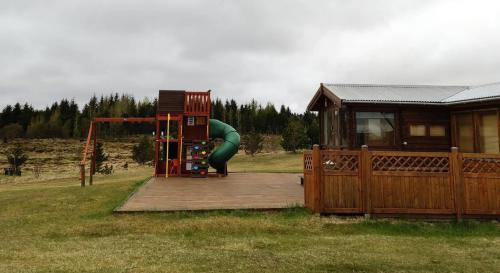 a playground with a green slide and a house at Cosy Cabin by Lake & Woods with Views in Selfoss