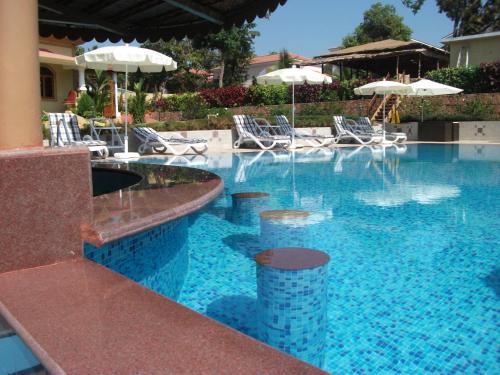 a swimming pool with chairs and umbrellas at Cochichos Resort in Vagator