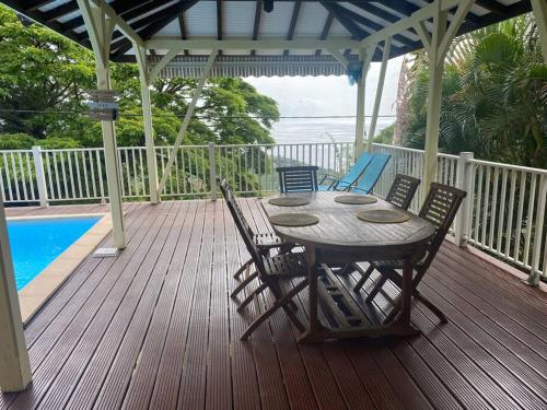 una terraza de madera con mesa y sillas junto a una piscina en Villa Petitparadis, en Le Carbet