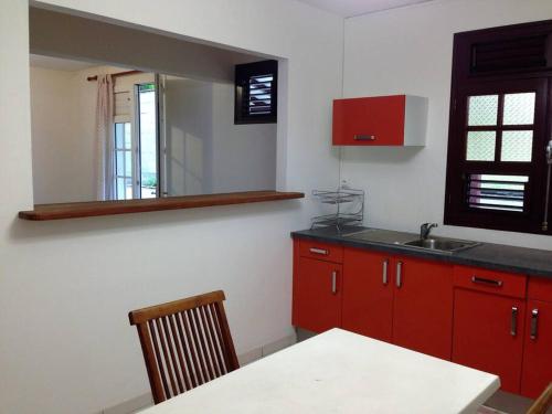 La cuisine est équipée de placards rouges, d'un lavabo et d'un miroir. dans l'établissement Appt Mer'Pelée, à Saint-Pierre